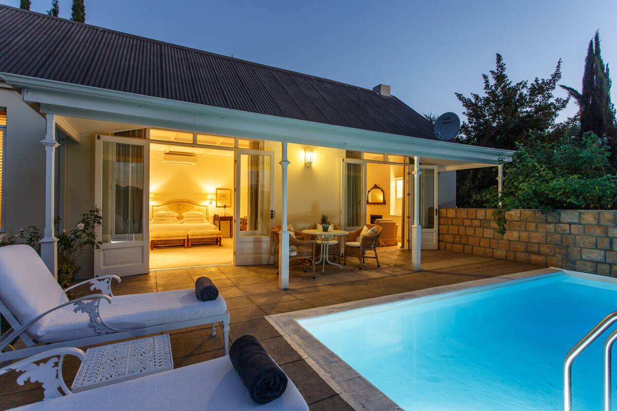 A poolside area with lounge chairs, a dining table, and a bedroom with a bed and nightstand.