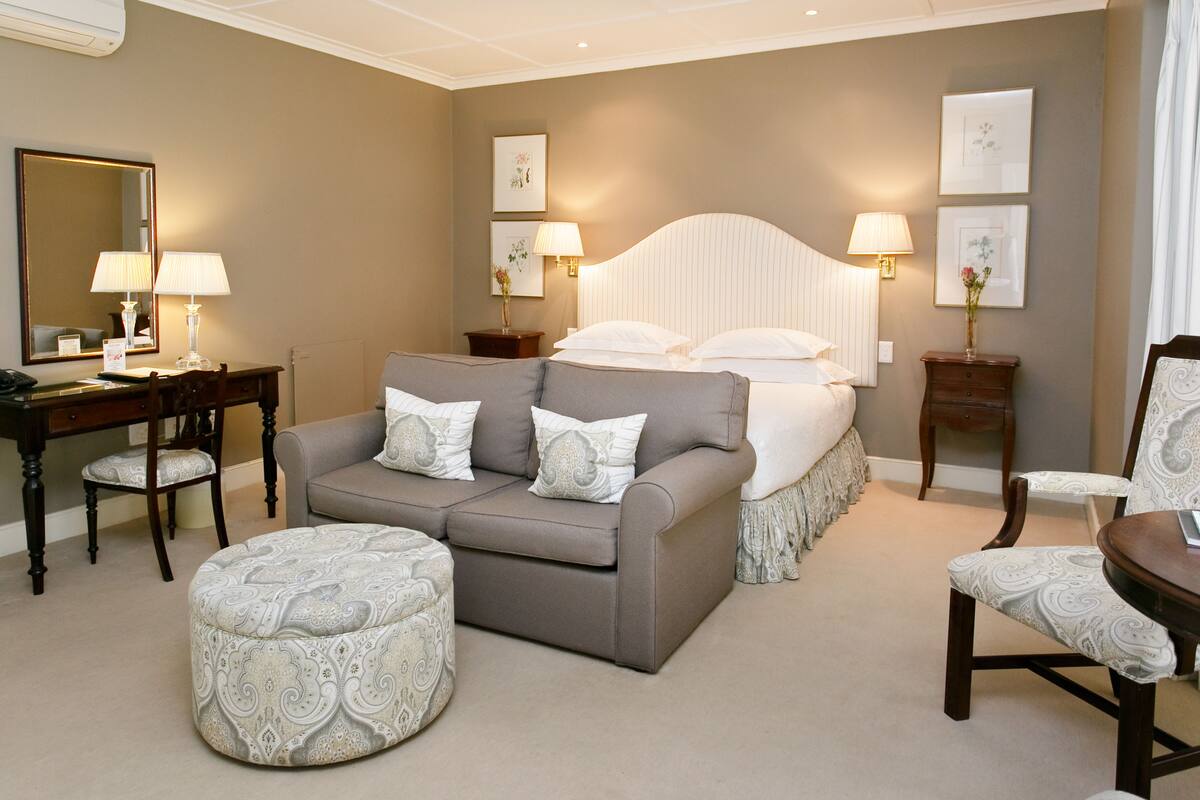 A hotel room with a bed, a sofa, a chair, a desk, and a mirror.