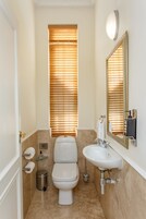 A compact bathroom with a toilet, sink, and window with blinds.
