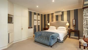 A bedroom with a large bed, a chest of drawers, a blue sofa, and a nightstand with a lamp.