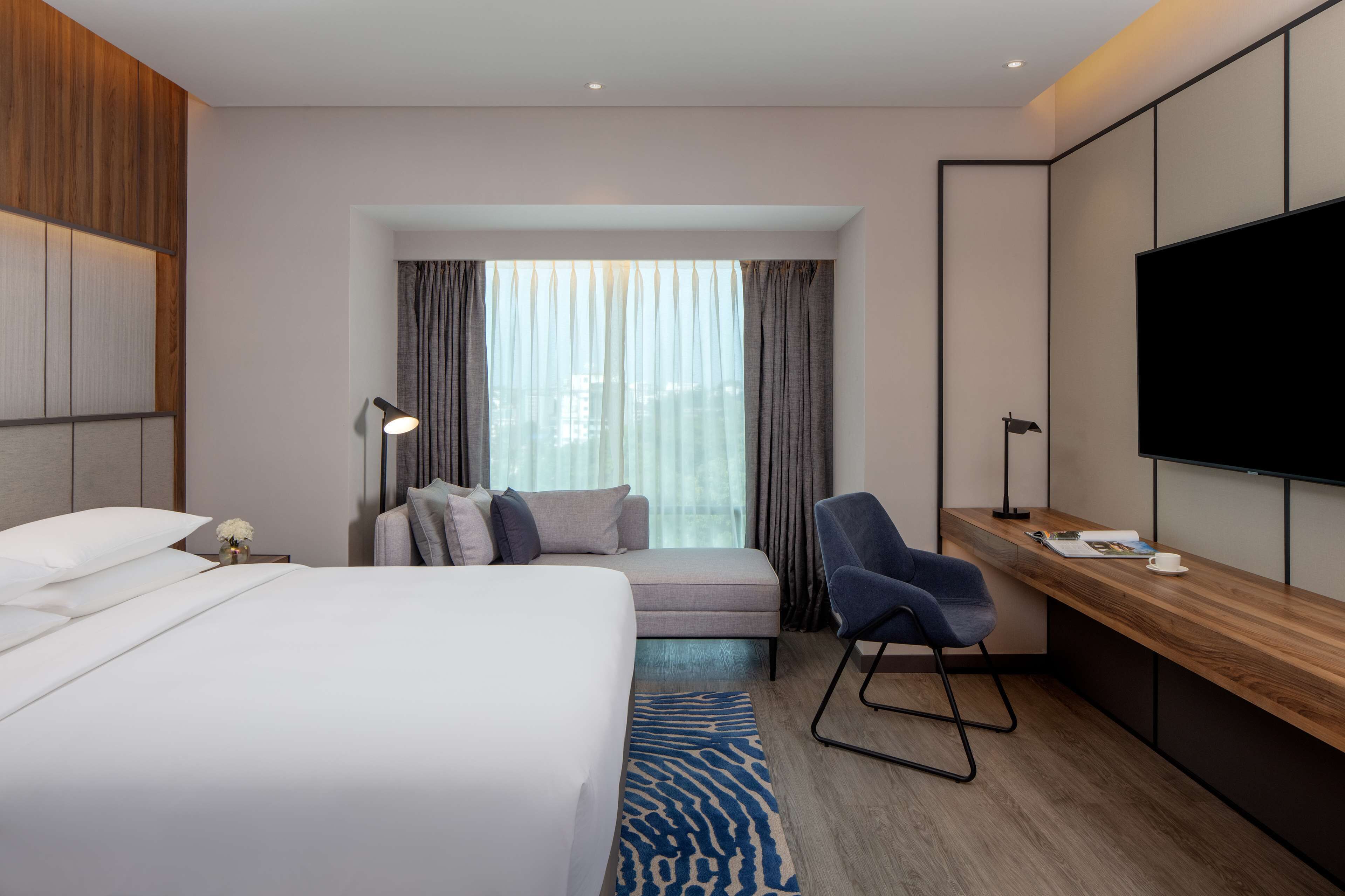 A hotel room with a bed, a desk, a chair, a TV, and a window with curtains.