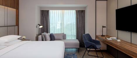 A hotel room with a bed, a desk, a chair, a TV, and a window with curtains.