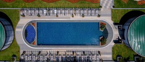 An aerial view of a swimming pool surrounded by a fence, with seating areas and a landscaped garden.