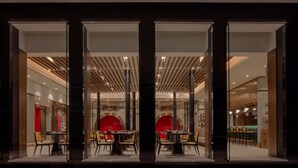 A modern restaurant with a glass facade, interior seating, and a central red archway. - Hyatt Regency Trivandrum (Thiruvananthapuram)
