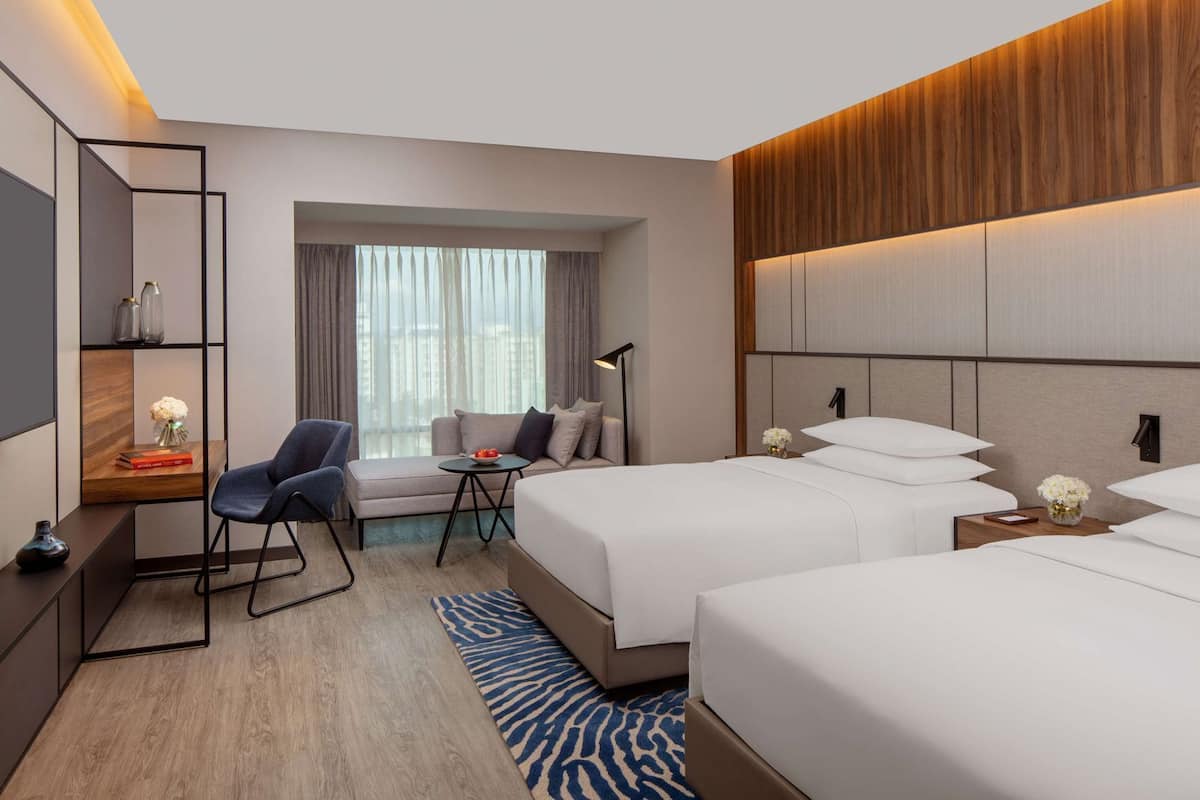 Une chambre d’hôtel avec un canapé, deux lits, une petite table, une chaise et une lampe.