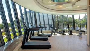 A modern gym with large windows, exercise equipment, and a unique ceiling design. - Hyatt Regency Trivandrum (Thiruvananthapuram)