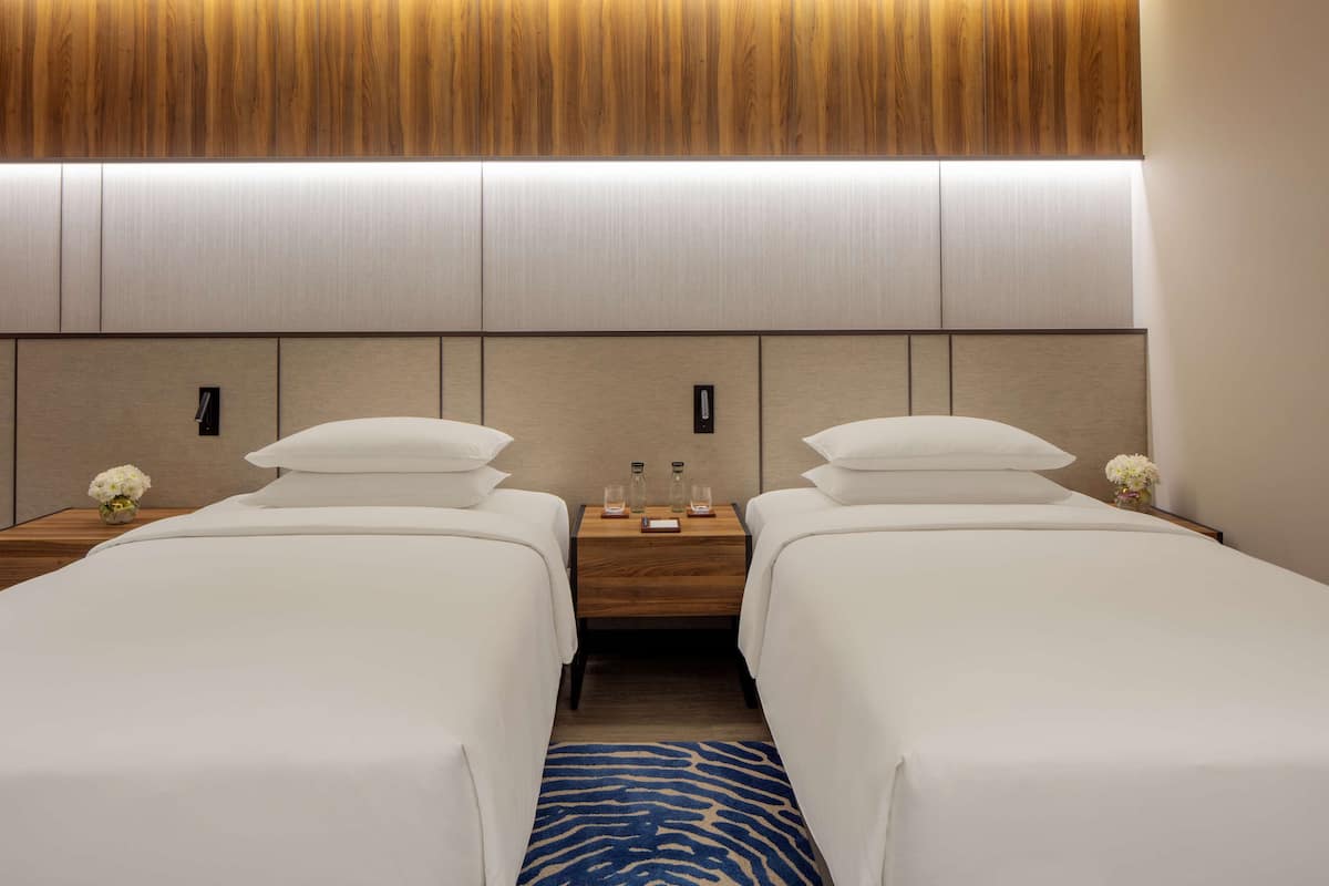 Une chambre d’hôtel avec deux lits simples, une table de chevet en bois avec une lampe et un tapis bleu à motifs.