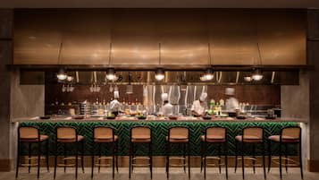 Una cocina moderna con una barra alargada, taburetes y tres cocineros trabajando.