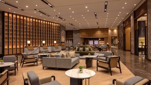A modern hotel lobby with a seating area, a reception desk, and a kitchen visible in the background. - Hyatt Regency Trivandrum (Thiruvananthapuram)