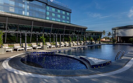 A modern hotel with a swimming pool, lounge chairs, and a clear blue sky.