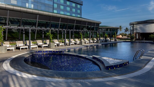 A modern hotel with a swimming pool, lounge chairs, and a clear blue sky. - Hyatt Regency Trivandrum (Thiruvananthapuram)