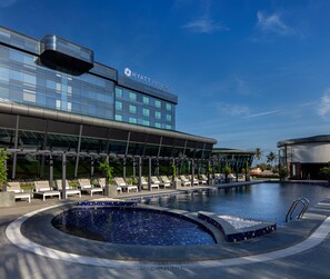 Un hotel moderno con piscina, sillas de descanso y un cielo azul despejado.