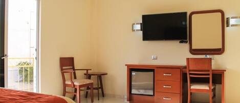 Una habitación de hotel con cama, escritorio con televisor, una silla y una mesita.