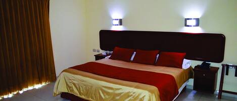 Una cama bien hecha con una colcha roja y dorada, dos lámparas de noche y una mesita de noche con lámpara.