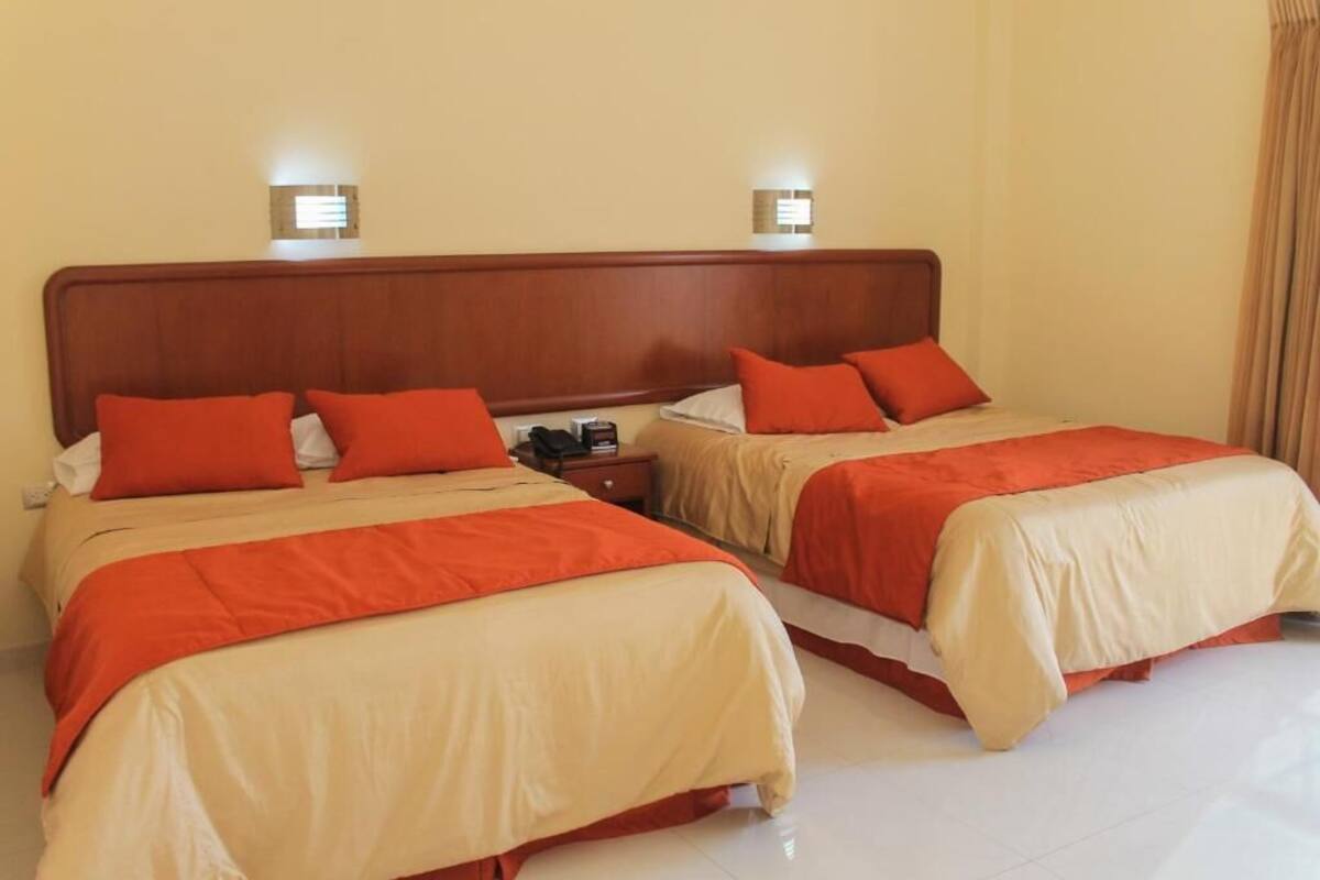 Una habitación de hotel con dos camas, cada una con ropa de cama roja y color crema, y lámparas de noche.
