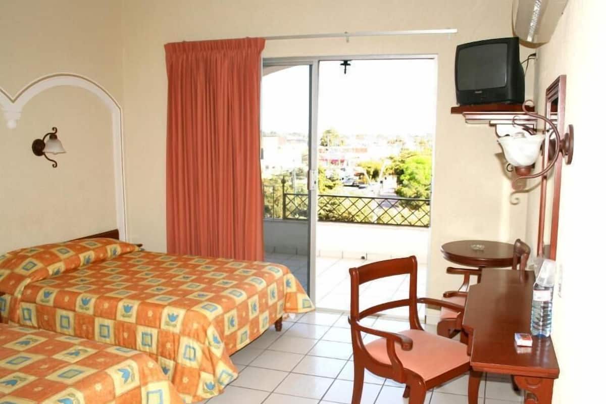 Habitación de hotel con dos camas, una mesita, una silla, televisor y balcón con vistas.