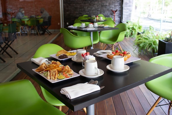Comedor con sillas y mesas verdes, mostrando una variedad de platos y una taza de café.