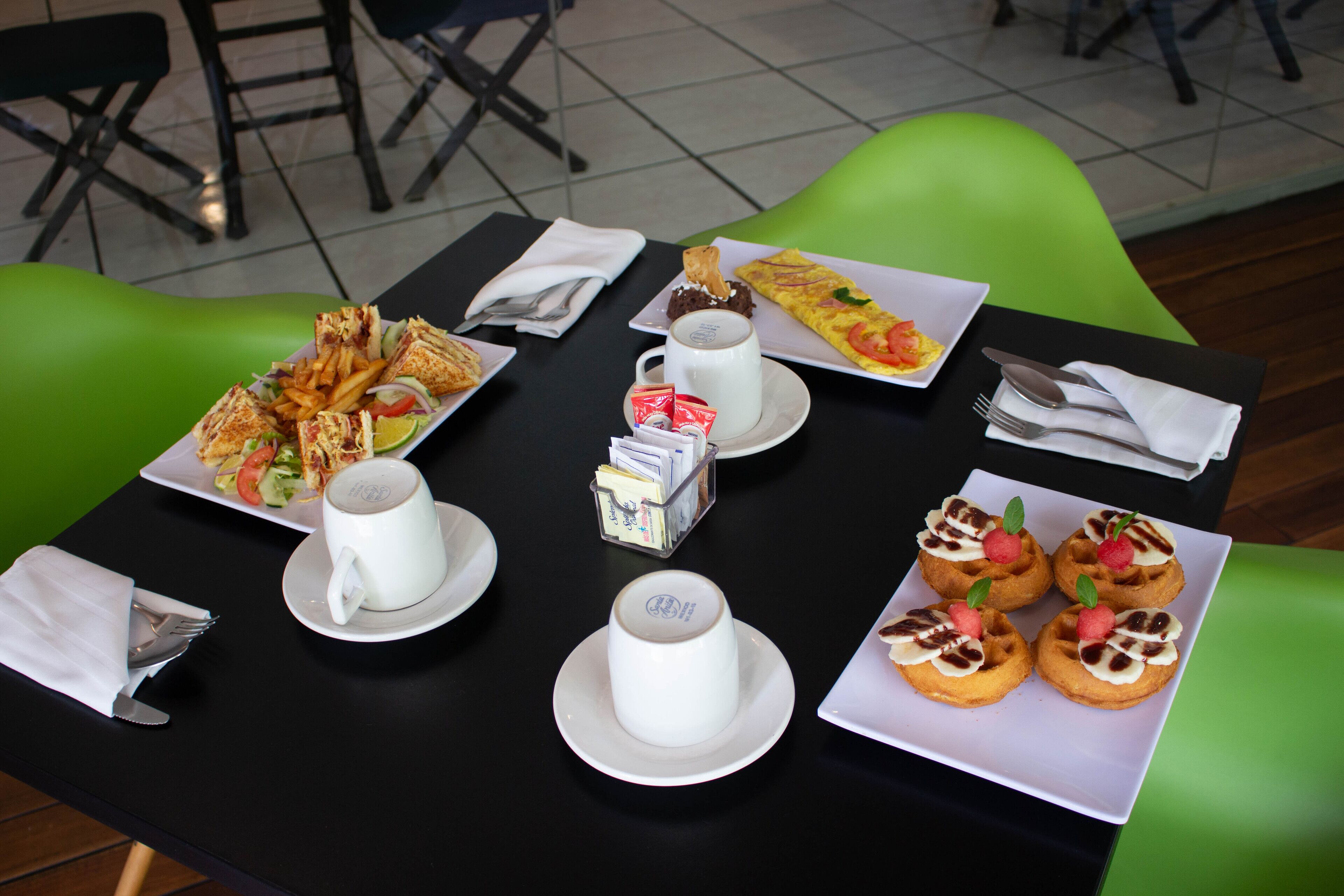 Una mesa servida con diversos alimentos para el desayuno, como sándwiches, una taza de café y pasteles.