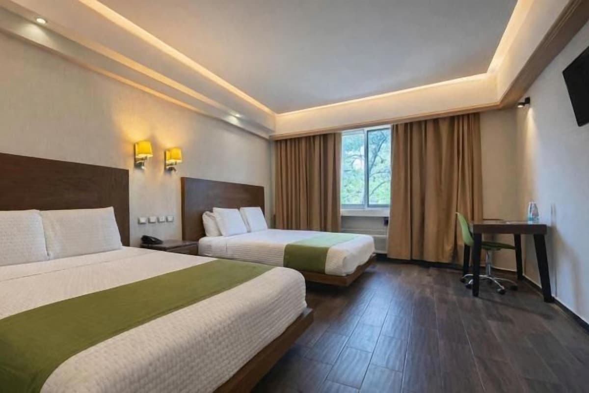 A hotel room with two beds, a desk, a chair, and a TV on the wall.