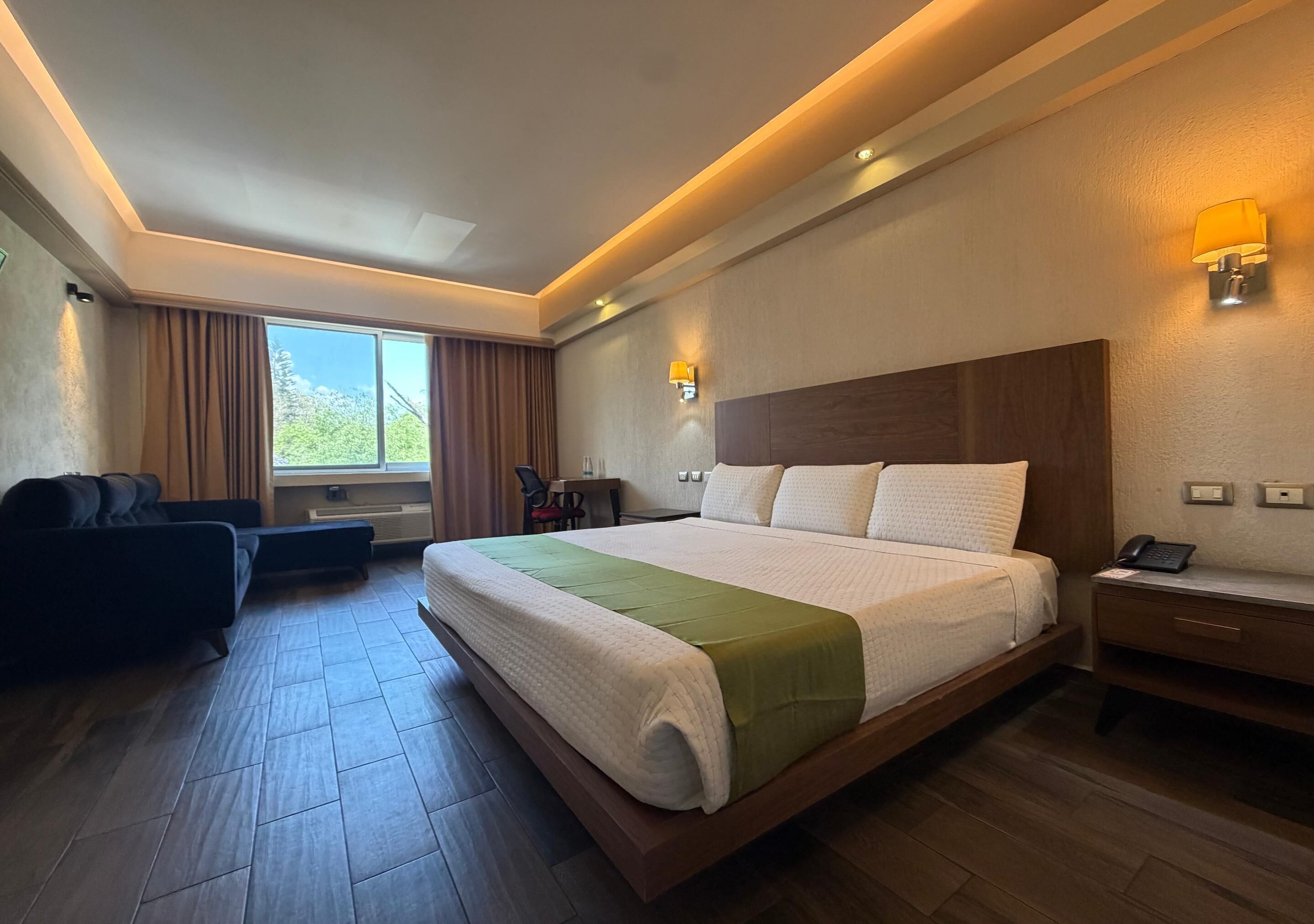 A hotel room with a large bed, a sofa, a desk, and a chair.