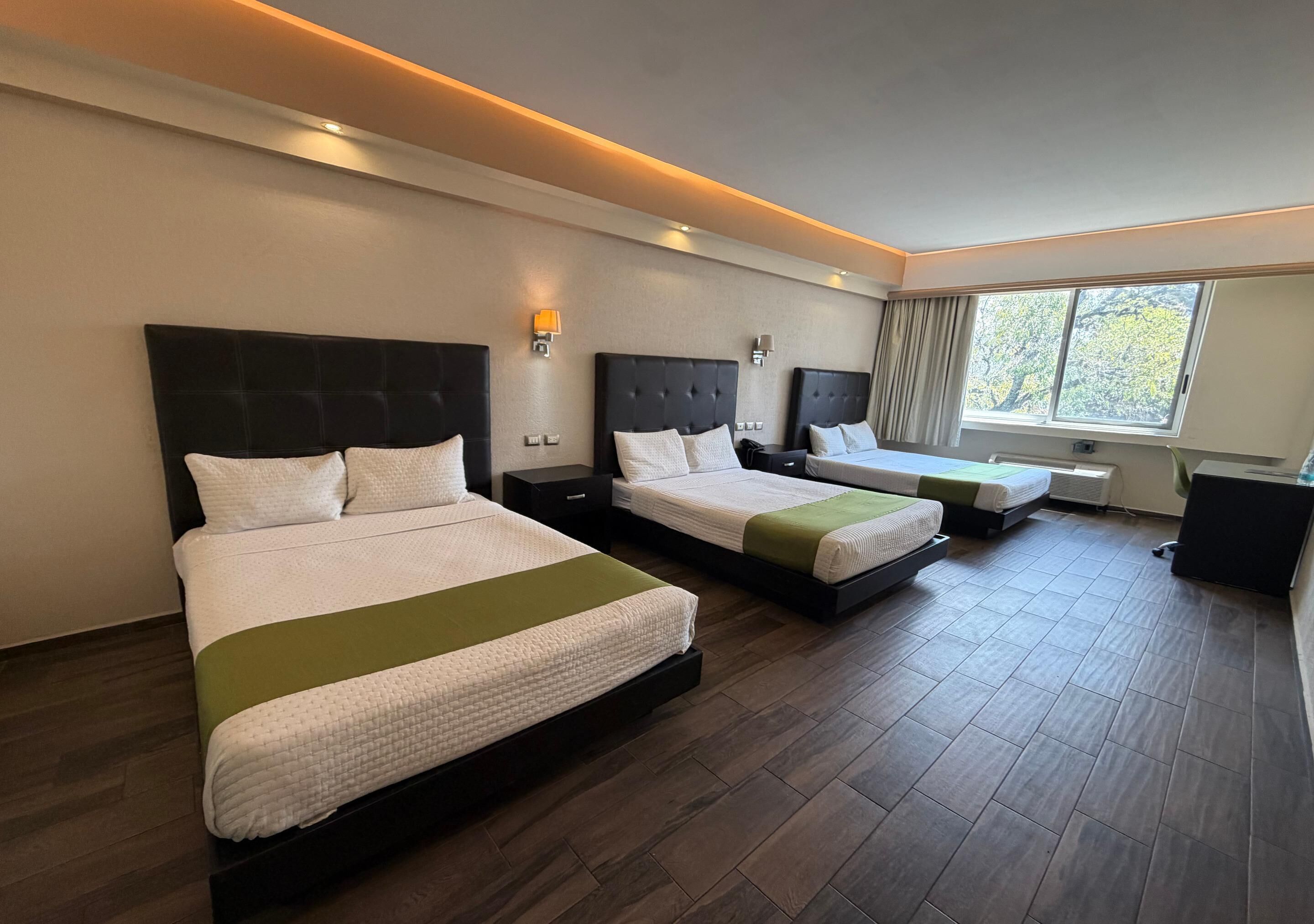 A hotel room with two beds, a desk, a chair, and a window with curtains.
