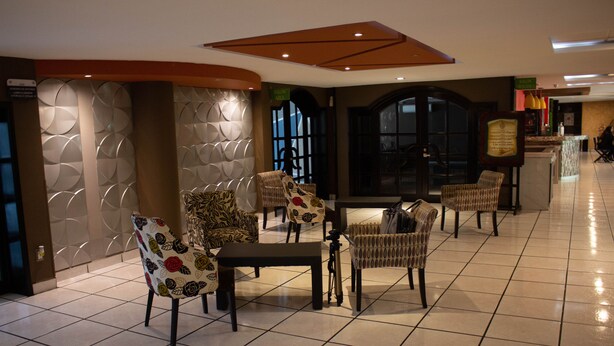 Un hall de hotel con una zona de estar que incluye sillas estampadas y una mesa, un ventanal grande y un letrero que indica un salón.