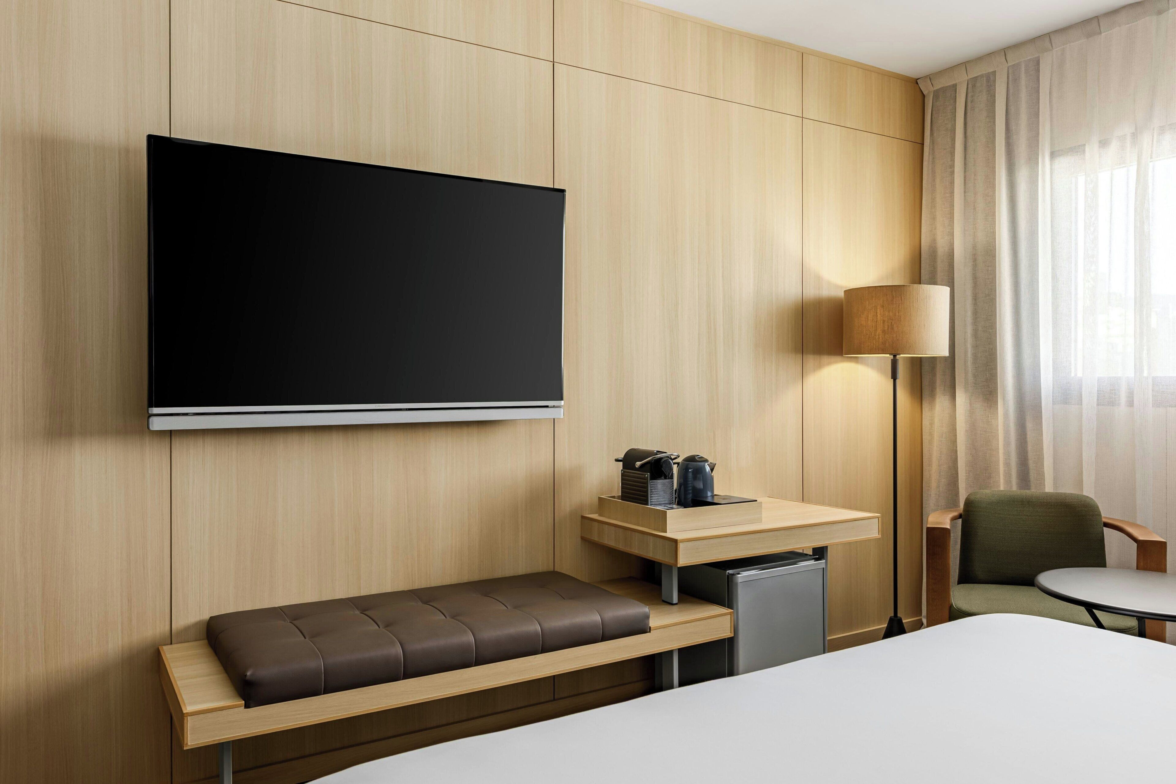 Een hotelkamer met een bed, een bankje, een televisie, een bureau, een lamp en een stoel.