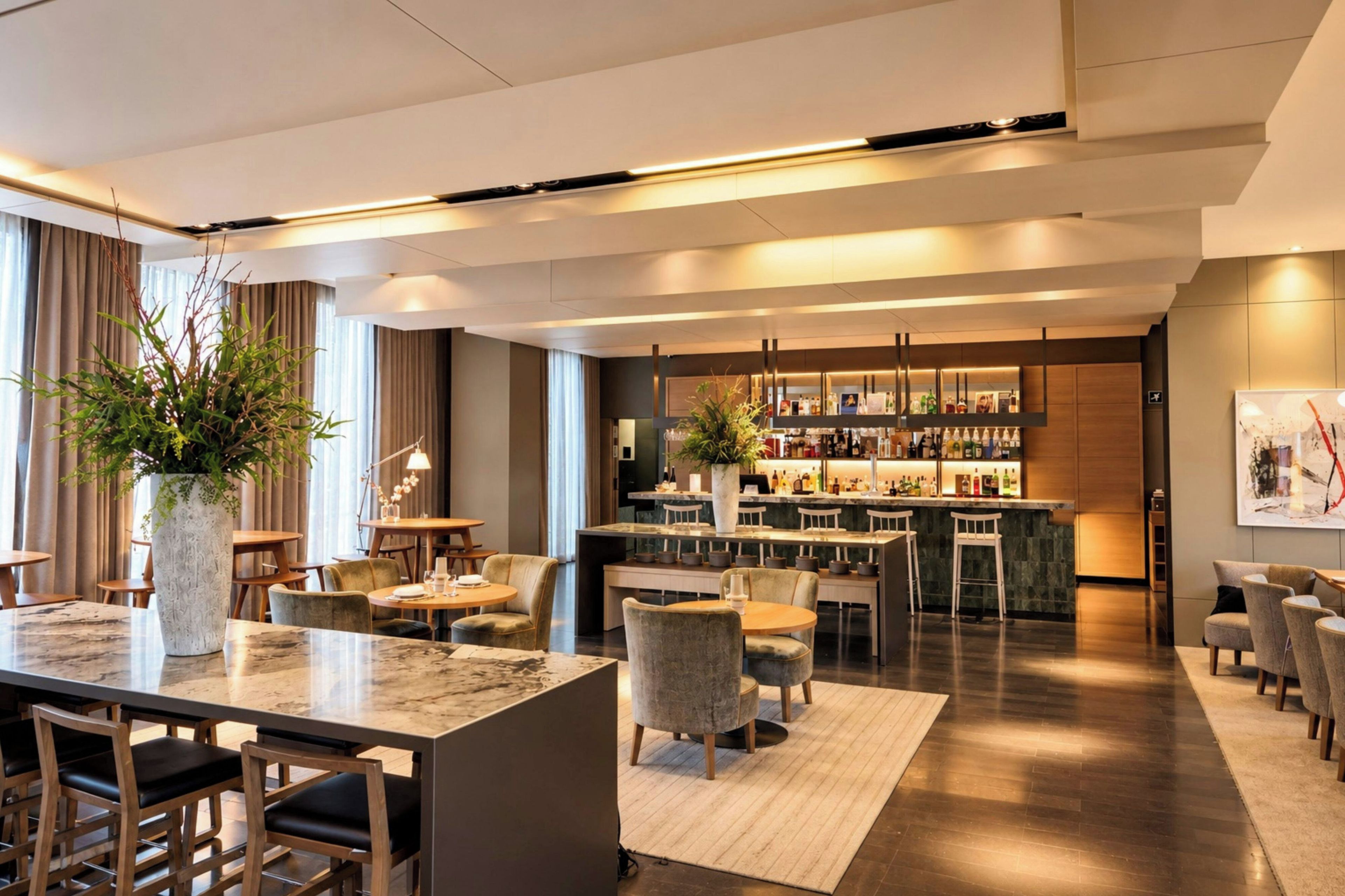 A modern hotel lobby with a bar area, seating arrangements, and a large vase with greenery.