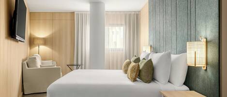 Habitación de hotel con cama, sofá, televisión, lámpara y luz empotrada en la pared.