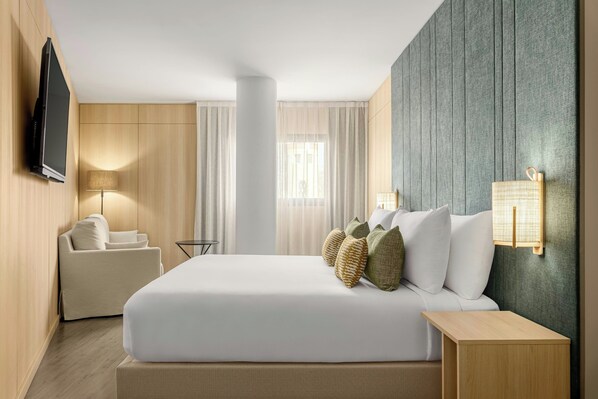 A hotel room with a bed, a sofa, a TV, a lamp, and a wall-mounted light.