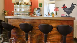 A bar area with four stools, a counter with a television, and shelves with bottles and glasses. - Hahn Hotel Vienna City (Vienna)
