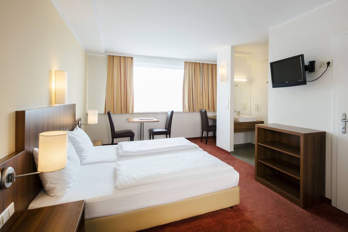 A hotel room with a bed, a desk, a chair, a television, and a small table.