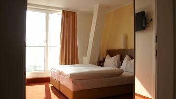 A hotel room with a bed, a TV, and a window with curtains.