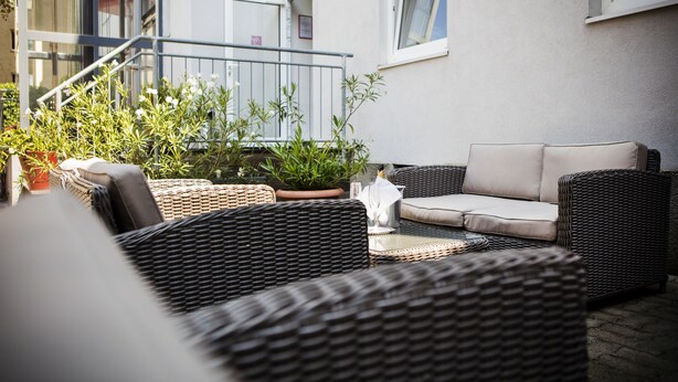 An outdoor seating area with wicker furniture, a potted plant, and a staircase leading to an upper level. - Hahn Hotel Vienna City (Vienna)