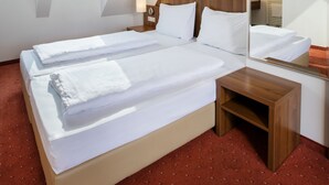 A hotel room with a large bed, a wooden nightstand, a mirror, and a TV mounted on the wall. - Hahn Hotel Vienna City (Vienna)
