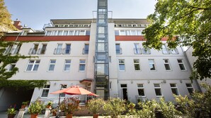 A multi-story building with a central glass elevator shaft, potted plants, and a red umbrella. - Hahn Hotel Vienna City (Vienna)