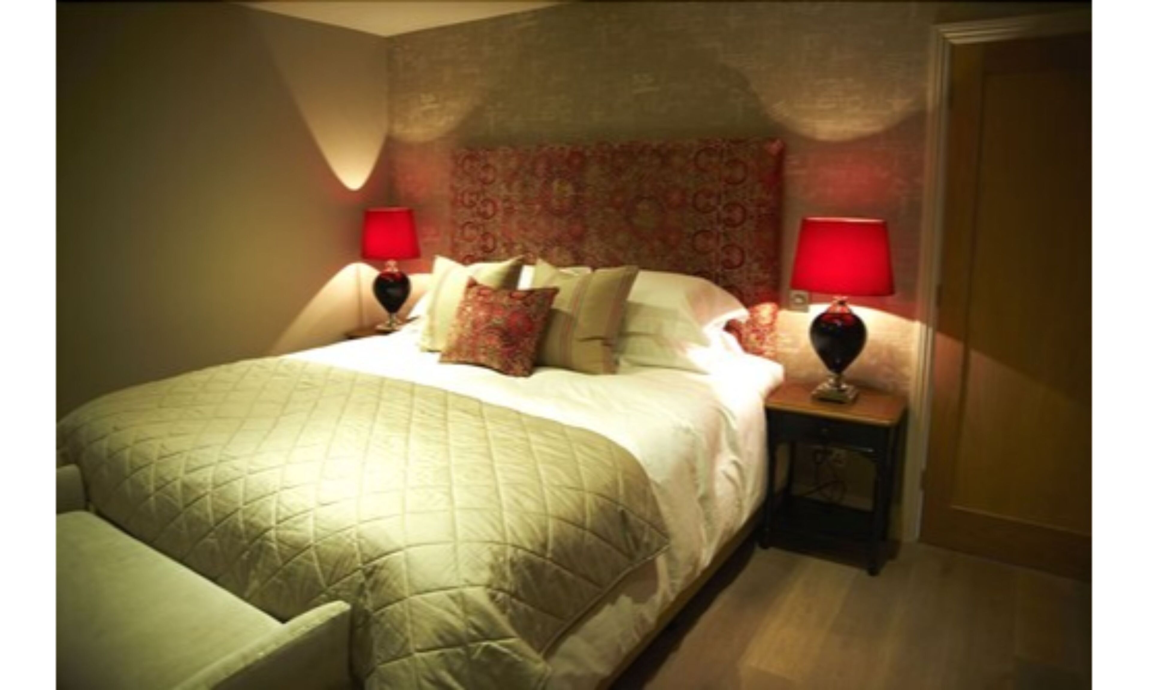 Cama bem arrumada com cobertura acolchoada, duas luminárias de cabeceira e painel de cama estampado.
