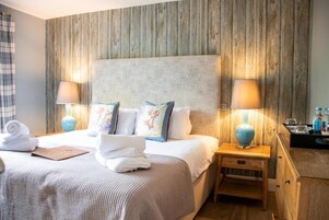 Habitación de hotel con una cama grande, dos mesitas de noche con lámparas, un cabecero de madera y un pequeño mueble de madera.