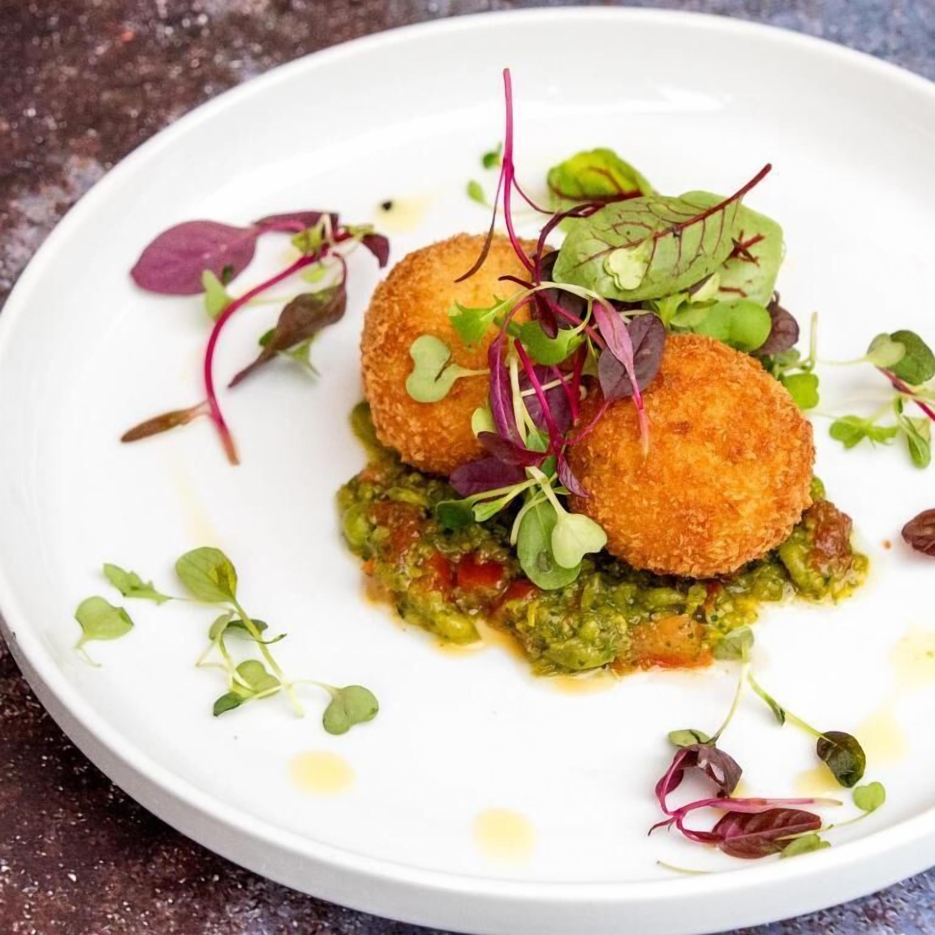 Un plat blanc amb dues amanides daurades, salsa verda i diverses fulles verdes petites.