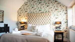 Hotelkamer met een groot bed, twee nachtkastjes met lampen, een decoratief paardbeeldje en een muur met een vogelmotief.