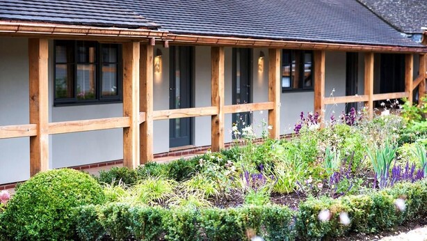 Een gebouw met een houten gevel, grote ramen en een verzorgde tuin met diverse planten en struiken.