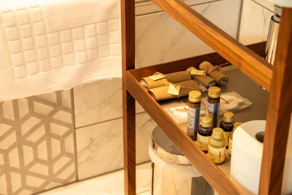 A bathroom with a wooden shelf holding toiletries and a roll of toilet paper.