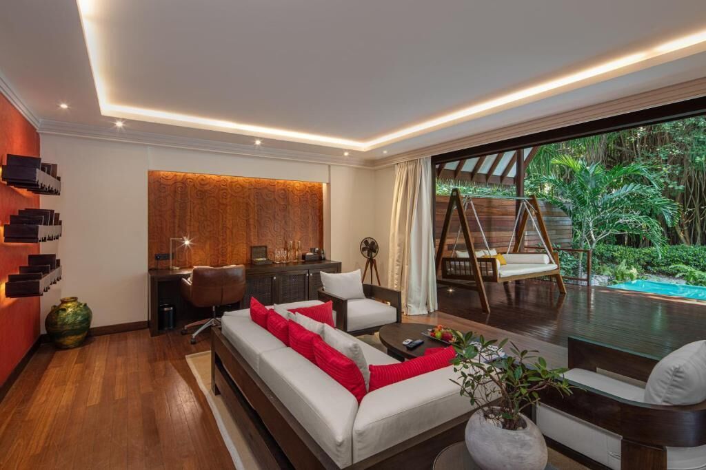 Ein modernes Wohnzimmer mit einer Couch, Sesseln, einem Couchtisch und Blick auf einen Pool und Grünflächen.