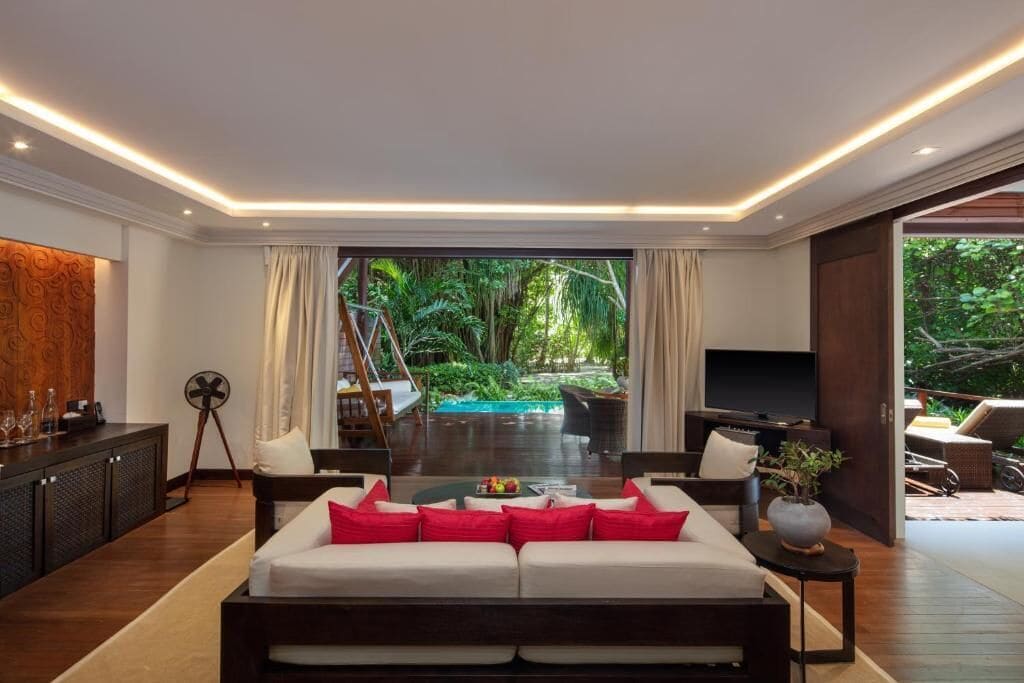 A modern living room with a sofa, a TV, and a view of a lush garden.