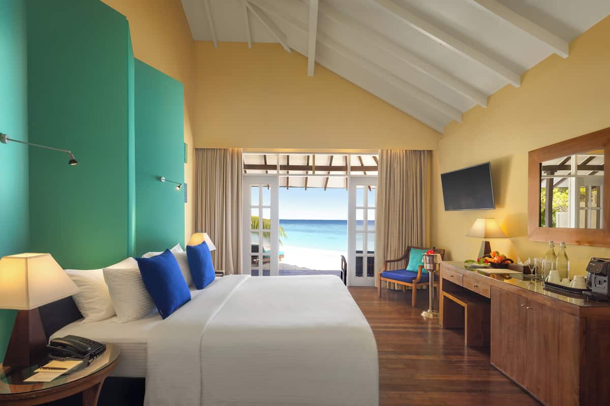 A hotel room with a bed, a desk, a chair, a TV, and a view of the beach.