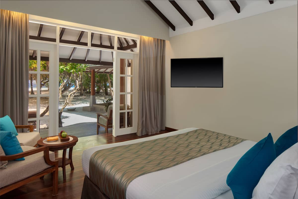 A hotel room with a bed, a seating area with a table, a TV mounted on the wall, and a view of the outdoors.
