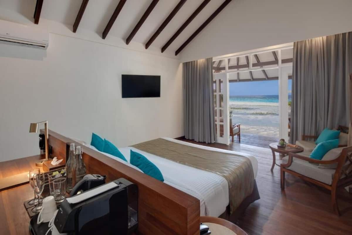 A hotel room with a bed, a desk with a computer, a TV, and a view of the beach.
