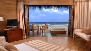 Ein Hotelzimmer mit einem großen Bett, einem Fernseher, einem Essbereich mit Tisch und Stühlen sowie Meerblick.