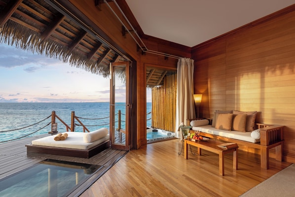 Una habitación con piso de vidrio, muebles de madera, un sofá y vista al océano.