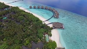 Eine Vogelperspektive zeigt ein Resort mit überwasserbungalows, einem Strand und einem Schwimmbecken.